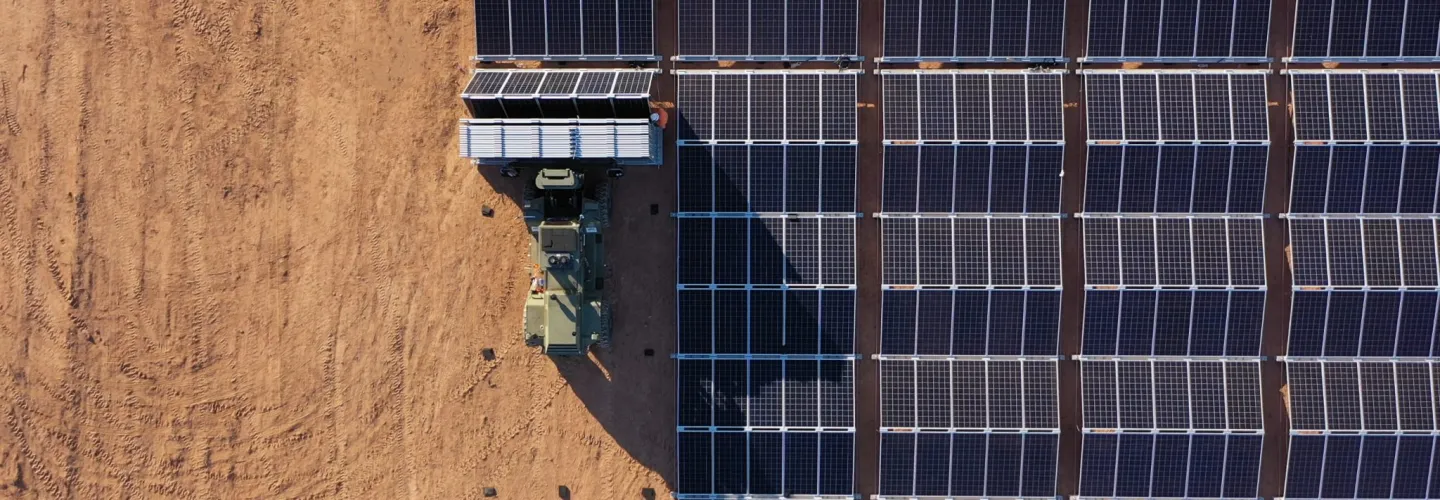 Aerial view of a solar panel installation in a desert area with a vehicle transporting additional panels.